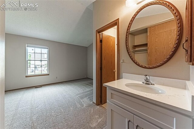 bathroom with a textured ceiling, vanity, and lofted ceiling