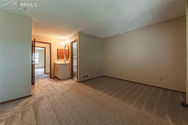 unfurnished bedroom with light colored carpet, sink, ensuite bath, and a textured ceiling