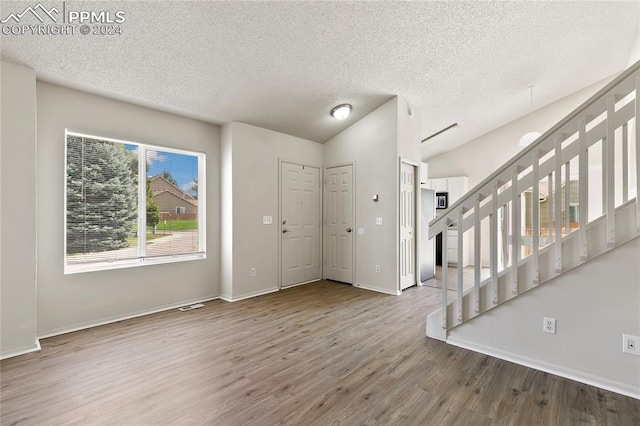 foyer entrance with vaulted ceiling, a textured ceiling, and hardwood / wood-style floors