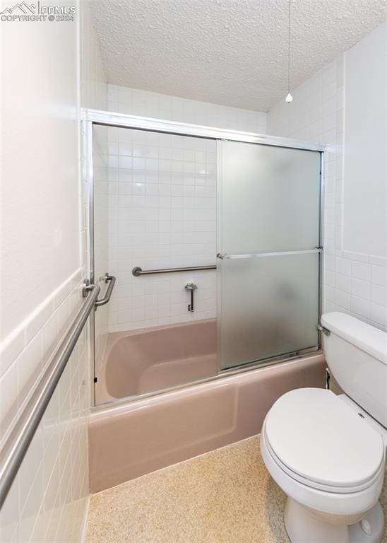 bathroom featuring tile walls, toilet, combined bath / shower with glass door, and a textured ceiling