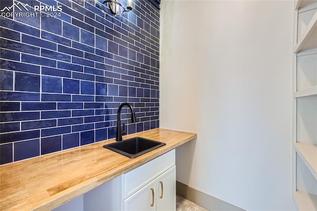 kitchen featuring butcher block countertops, tasteful backsplash, white cabinetry, and sink