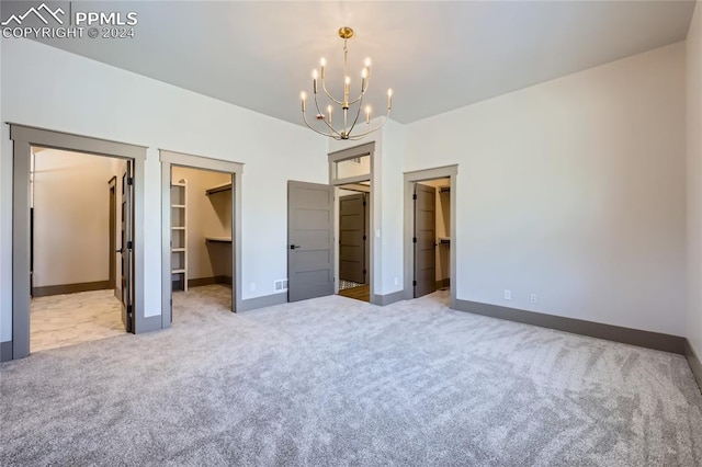 unfurnished bedroom with a chandelier, light colored carpet, a spacious closet, and a closet