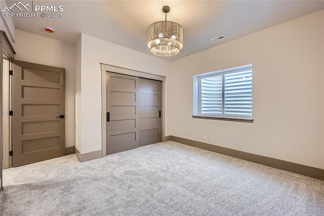 unfurnished bedroom with a closet, carpet floors, and an inviting chandelier