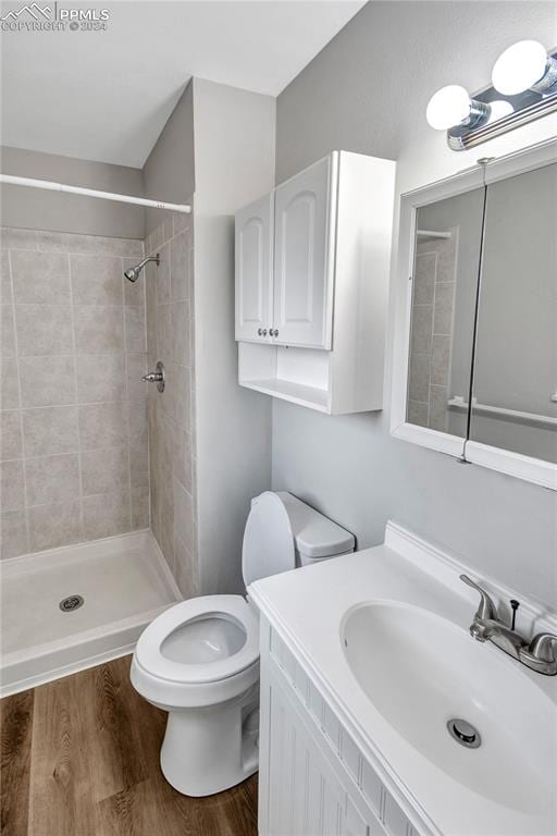 bathroom with wood-type flooring, vanity, toilet, and a tile shower