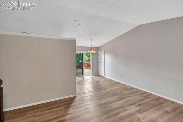 spare room featuring a chandelier, lofted ceiling, hardwood / wood-style floors, and a textured ceiling