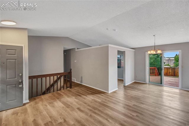 unfurnished room with a textured ceiling, a chandelier, vaulted ceiling, and wood-type flooring