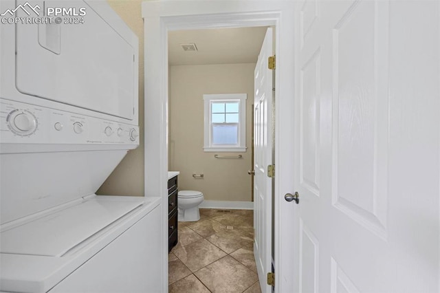 bathroom with toilet, stacked washer and clothes dryer, and tile patterned flooring