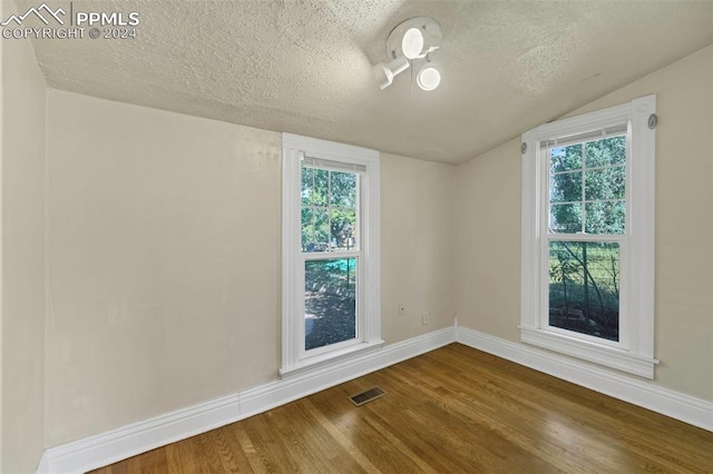 unfurnished room with a healthy amount of sunlight, wood-type flooring, vaulted ceiling, and a textured ceiling