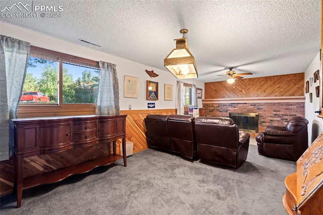 carpeted living room featuring wooden walls, ceiling fan, a fireplace, and a textured ceiling