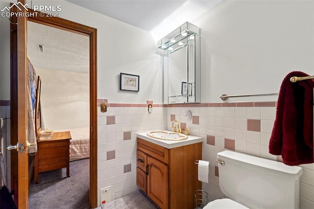 bathroom featuring a textured ceiling, tile walls, vanity, and toilet