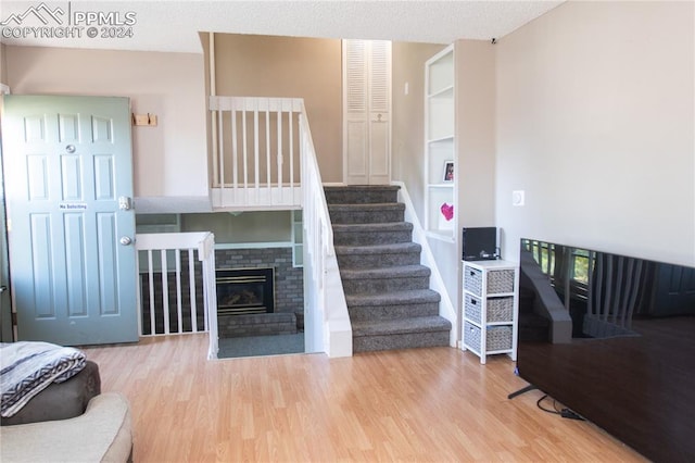 staircase featuring wood-type flooring, a textured ceiling, and a brick fireplace