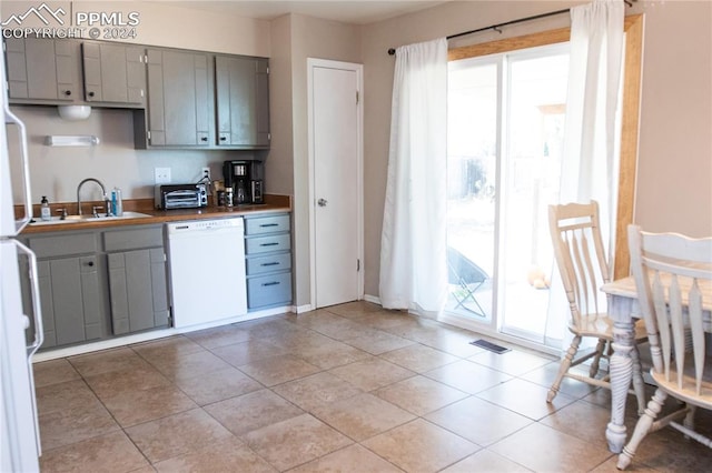 kitchen featuring gray cabinetry, white dishwasher, butcher block countertops, and a wealth of natural light