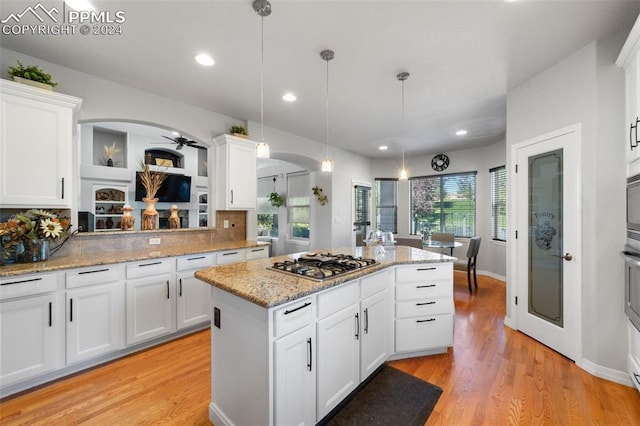 kitchen with light hardwood / wood-style floors, white cabinetry, stainless steel gas cooktop, a center island, and decorative light fixtures