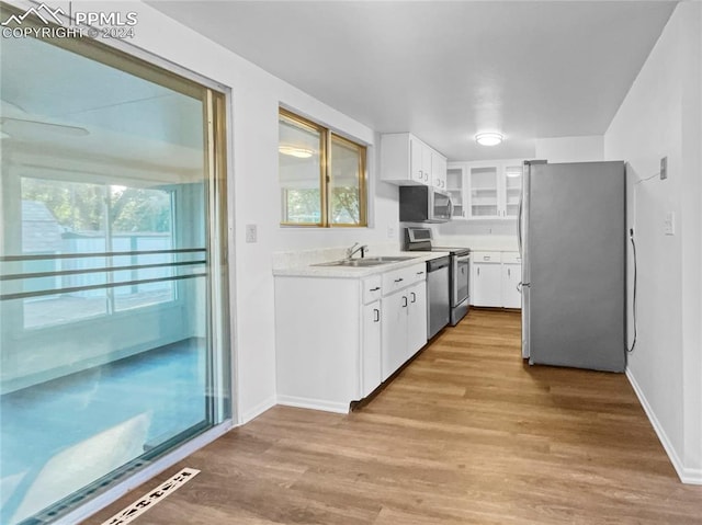 kitchen with plenty of natural light, appliances with stainless steel finishes, white cabinets, and light hardwood / wood-style floors