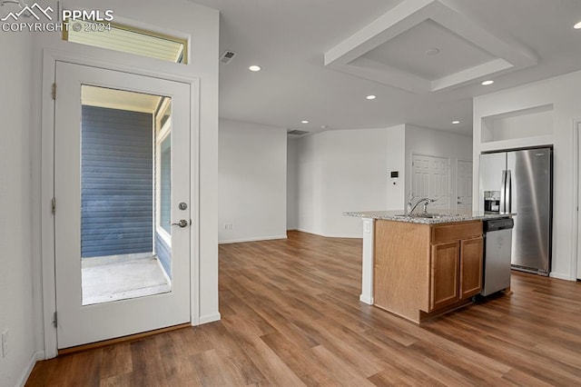 kitchen with a kitchen island with sink, a raised ceiling, appliances with stainless steel finishes, hardwood / wood-style floors, and light stone countertops