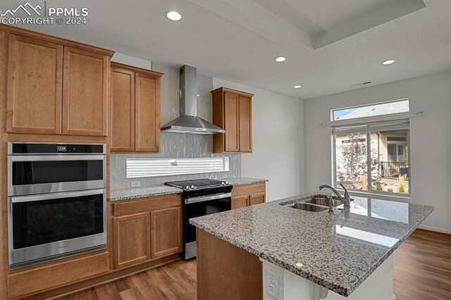 kitchen with wall chimney exhaust hood, a breakfast bar area, stainless steel appliances, wood-type flooring, and a kitchen island with sink