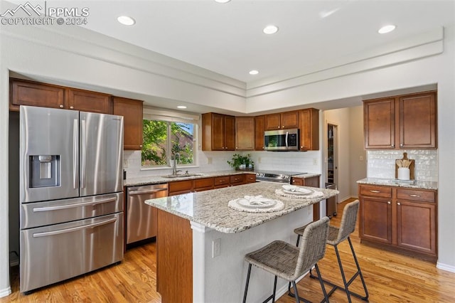 kitchen featuring appliances with stainless steel finishes, a kitchen breakfast bar, a center island, light hardwood / wood-style flooring, and sink