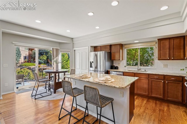 kitchen featuring appliances with stainless steel finishes, backsplash, a kitchen island, light stone countertops, and light hardwood / wood-style flooring