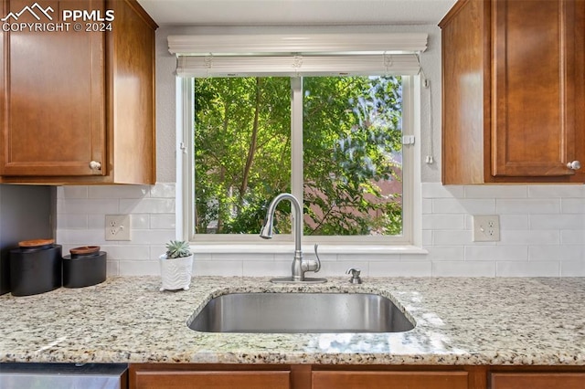 kitchen featuring light stone countertops, black dishwasher, tasteful backsplash, and sink