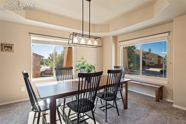 carpeted dining room featuring a chandelier and a raised ceiling