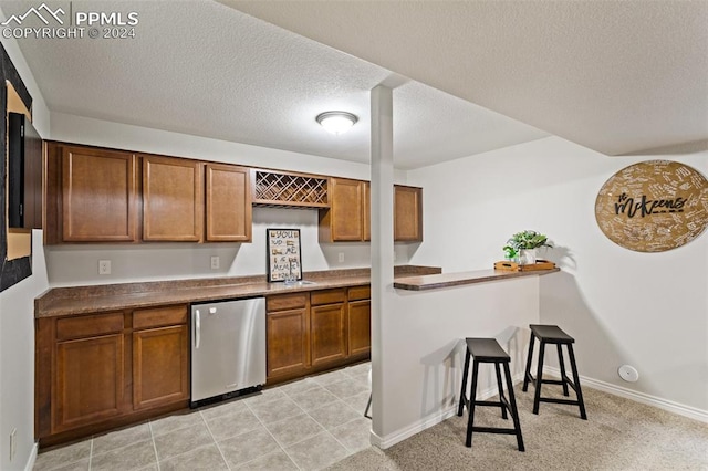 kitchen featuring a textured ceiling, stainless steel fridge, a breakfast bar area, and light colored carpet