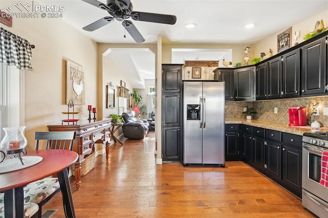 kitchen with appliances with stainless steel finishes, decorative backsplash, light stone counters, light wood-type flooring, and ceiling fan