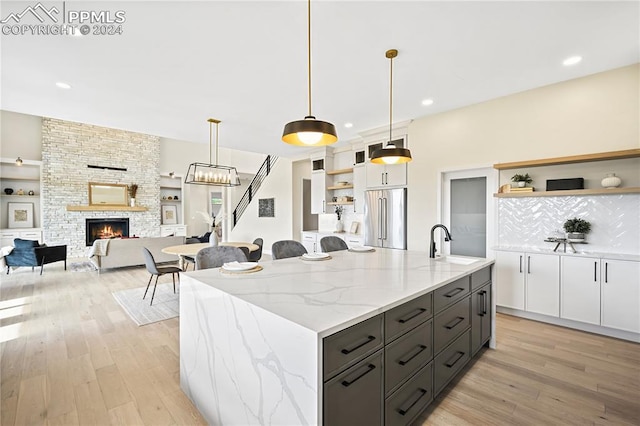 kitchen featuring white cabinetry, hanging light fixtures, a fireplace, a center island with sink, and high end fridge