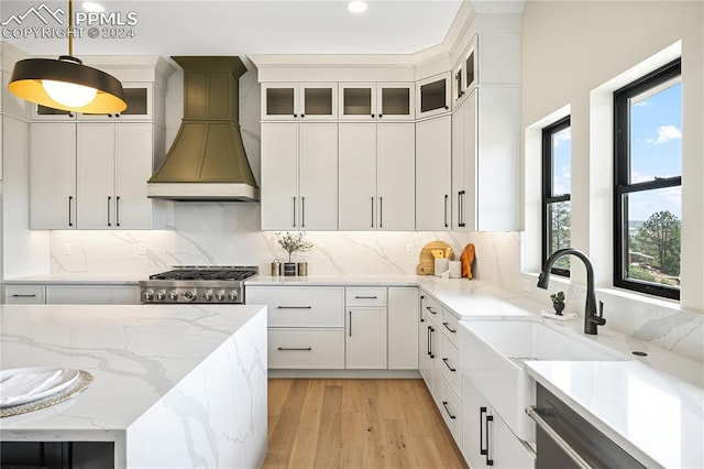 kitchen with light wood-type flooring, light stone counters, white cabinets, hanging light fixtures, and custom exhaust hood