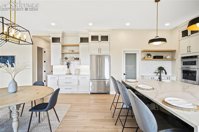 kitchen with appliances with stainless steel finishes, decorative light fixtures, light stone countertops, and white cabinets