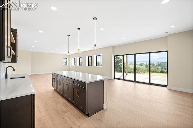 kitchen with pendant lighting, light wood-type flooring, sink, a kitchen island, and light stone countertops