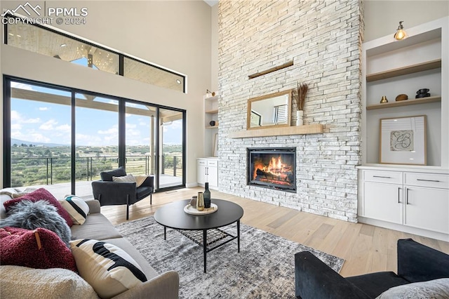 living room featuring built in shelves, a stone fireplace, light wood-type flooring, and a high ceiling