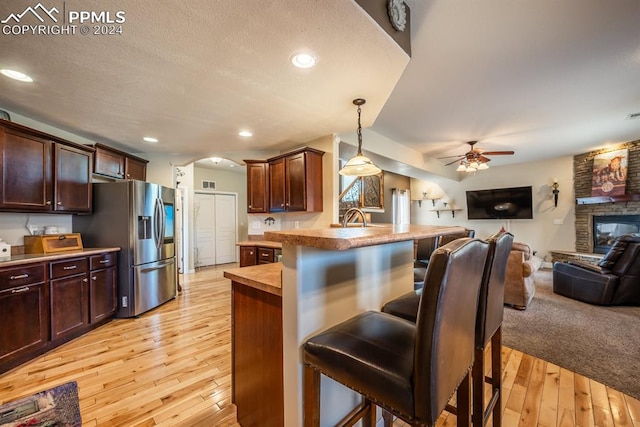 kitchen with light hardwood / wood-style floors, a stone fireplace, ceiling fan, and a breakfast bar