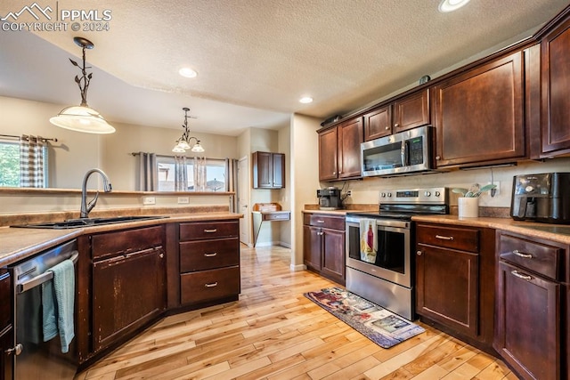 kitchen with pendant lighting, a textured ceiling, stainless steel appliances, and light wood-type flooring