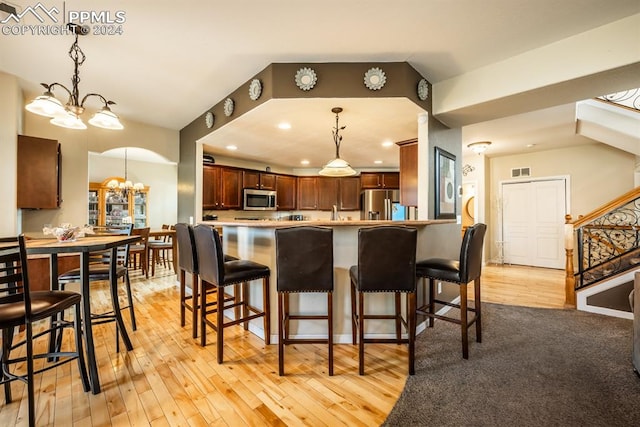 kitchen featuring pendant lighting, light wood-type flooring, a chandelier, kitchen peninsula, and appliances with stainless steel finishes