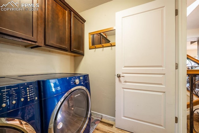 clothes washing area featuring light wood-type flooring, washing machine and clothes dryer, and cabinets