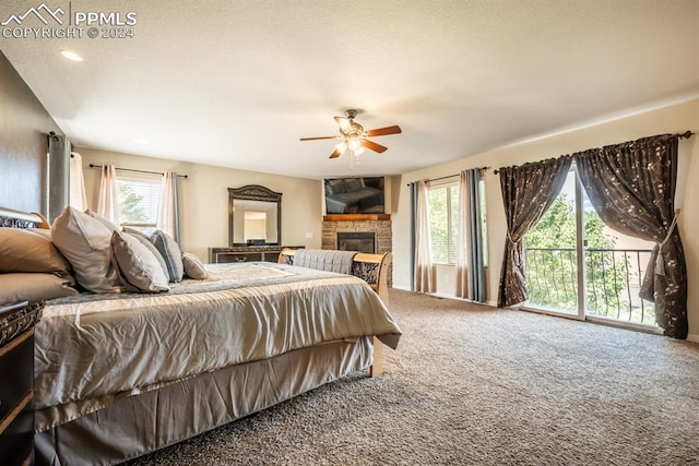 carpeted bedroom featuring multiple windows, access to outside, a stone fireplace, and ceiling fan