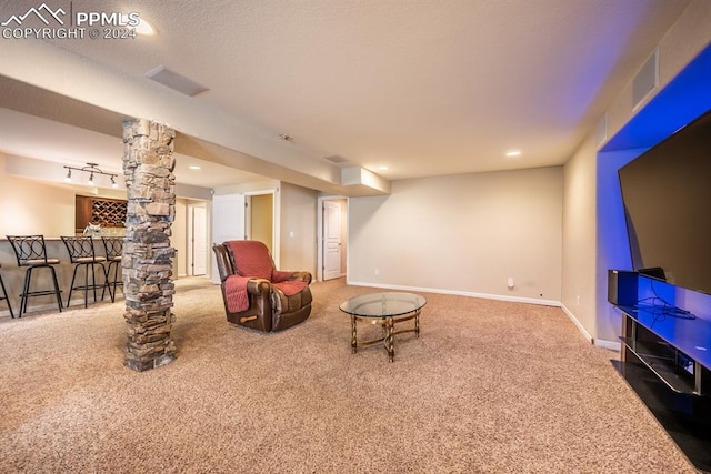 sitting room featuring a textured ceiling, track lighting, bar area, carpet flooring, and ornate columns