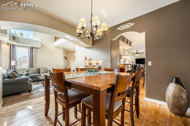 dining room featuring ceiling fan with notable chandelier, light hardwood / wood-style floors, and vaulted ceiling