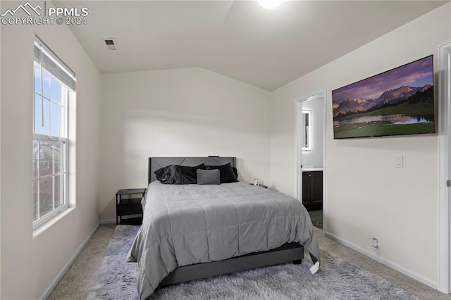 bedroom featuring lofted ceiling, light colored carpet, and ensuite bath