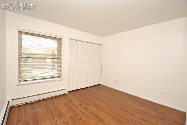 unfurnished bedroom featuring a baseboard radiator, a closet, and hardwood / wood-style floors