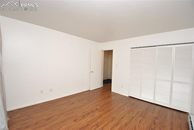 unfurnished bedroom featuring hardwood / wood-style flooring and a baseboard heating unit