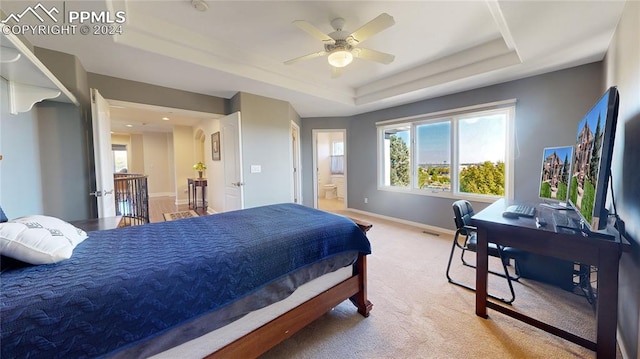 bedroom featuring ceiling fan, light colored carpet, a tray ceiling, and ensuite bath