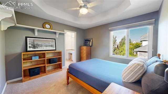 bedroom featuring light carpet, connected bathroom, a tray ceiling, and ceiling fan