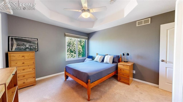 bedroom with a raised ceiling, light carpet, and ceiling fan