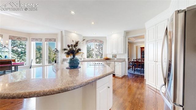 kitchen with stainless steel fridge, white cabinetry, a kitchen island, light stone countertops, and light wood-type flooring