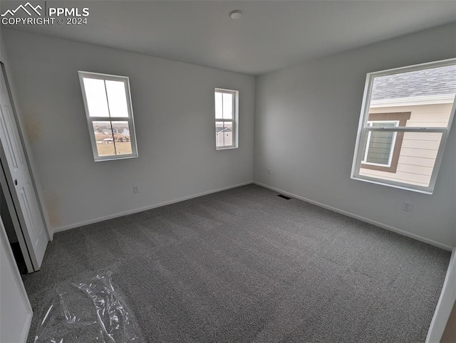 spare room featuring dark carpet and a wealth of natural light