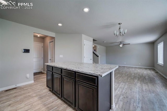 kitchen with light hardwood / wood-style floors, ceiling fan with notable chandelier, a kitchen island, pendant lighting, and dark brown cabinets