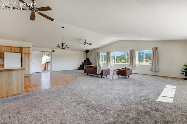 unfurnished living room with ceiling fan with notable chandelier, a wood stove, lofted ceiling, and light hardwood / wood-style flooring