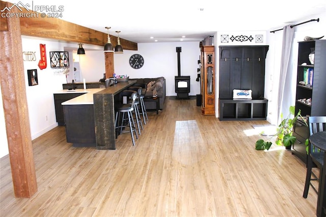 kitchen with kitchen peninsula, a wood stove, a kitchen bar, light hardwood / wood-style flooring, and decorative light fixtures