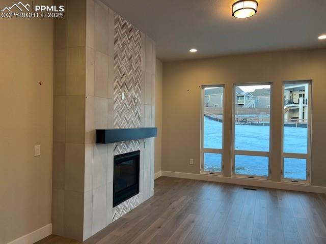 unfurnished living room featuring recessed lighting, baseboards, wood finished floors, and a tile fireplace